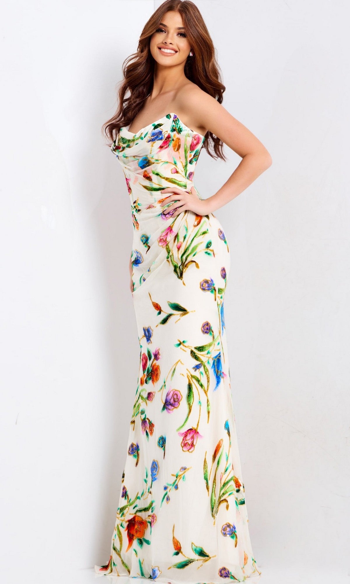 A woman poses in the Jovani 47626 long prom dress, featuring a strapless design with a vibrant floral print on ivory satin, set against a plain white background.